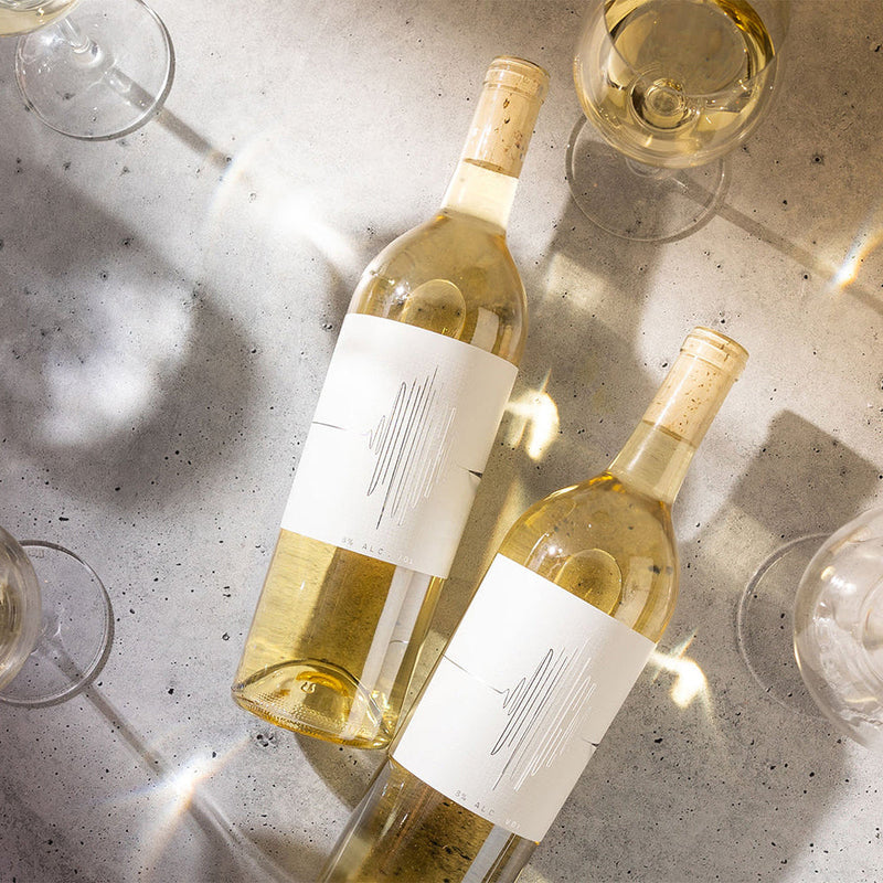 Two bottles of Divulge Low Alcohol White Wine laying on concrete surrounded by glasses of wine