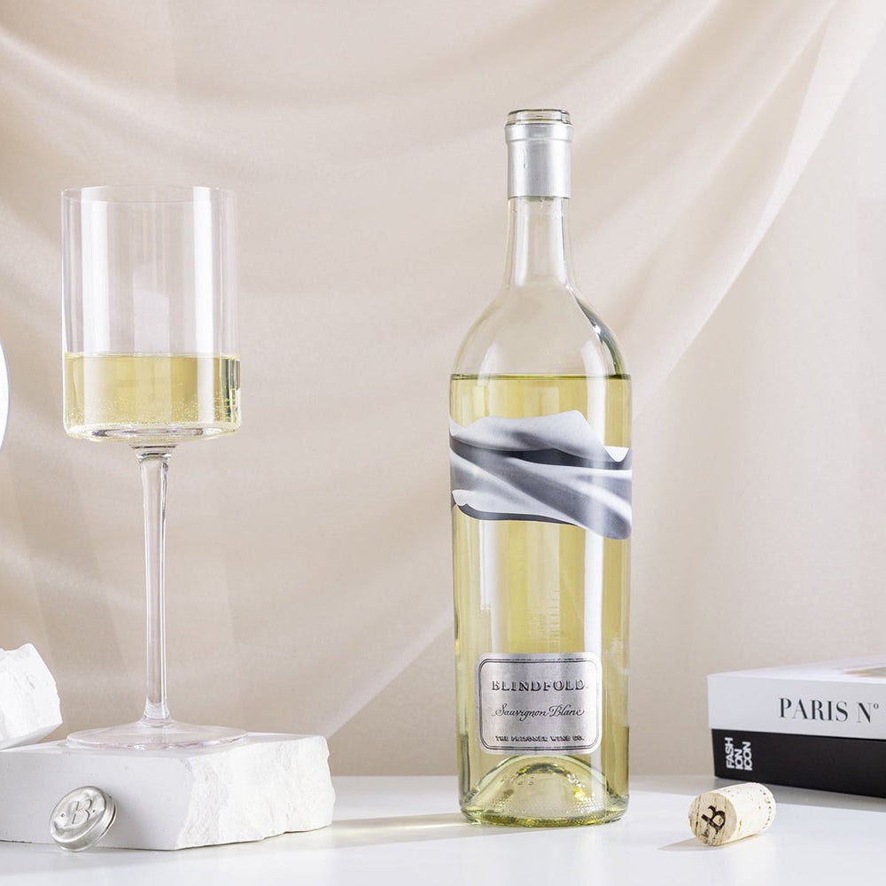 A bottle Blindfold Sauvignon Blanc with a wine glass against a draped cloth background