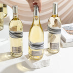 Three bottles of white wine with marble labels on a light surface.