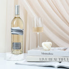 A bottle of Blindfold Blanc de Noir, books, and candle on a table with a soft curtain background
