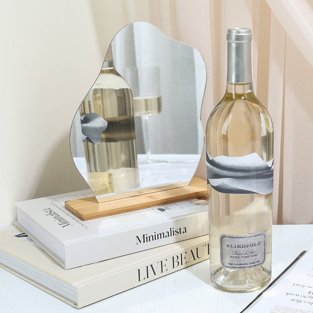 Bottle of white wine on a table with decorative items including a mirror, books, and a vase.