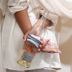 Person holding a bottle of Blindfold Blanc de Noir  and a wine glass with a white curtain in the background