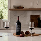 A bottle of Double Diamond : 2021 Napa Valley Proprietary Red Wine 750mL on a kitchen countertop with wine glasses and tomatoes on a cutting board