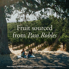 A scenic vineyard landscape with two people sitting under a large tree on the ground, overlaid with the text 'Fruit sourced from Paso Robles.'