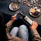 Person sitting at an outside with a bottle of Mount Veeder Winery Estate Merlot and a glass, surrounded by s'mores.