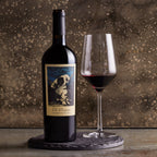 Wine bottle of The Prisoner Cabernet Sauvignon and a glass of red wine on a textured surface.