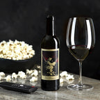 Wine bottle with label, wine glass, and bowl of popcorn on a dark background