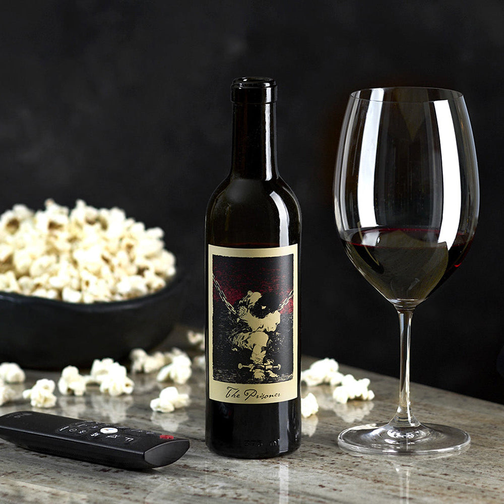 Wine bottle with label, wine glass, and bowl of popcorn on a dark background