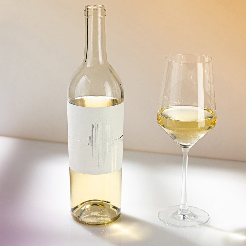 A bottle of Divulge Low Alcohol White Wine next to a wine glass on a light background