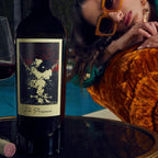 Wine bottle labeled 'The Prisoner' with a person wearing sunglasses laying on an orange sofa in the background.