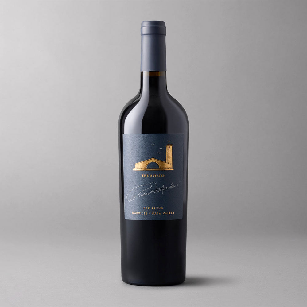 A bottle of Robert Mondavi Winery The Estates Red Blend Oakville, featuring a dark slate blue label with a gold arch & tower illustration and white script, set against a gray background.
