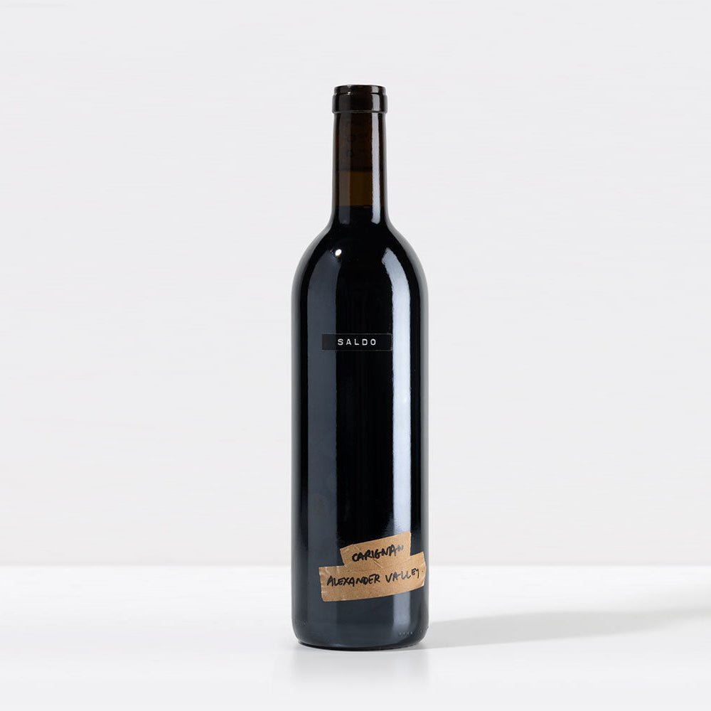 Wine bottle with a black label 'SALDO' and 'Carignan Alexander Valley' on tape at the bottom of the bottle on a white background
