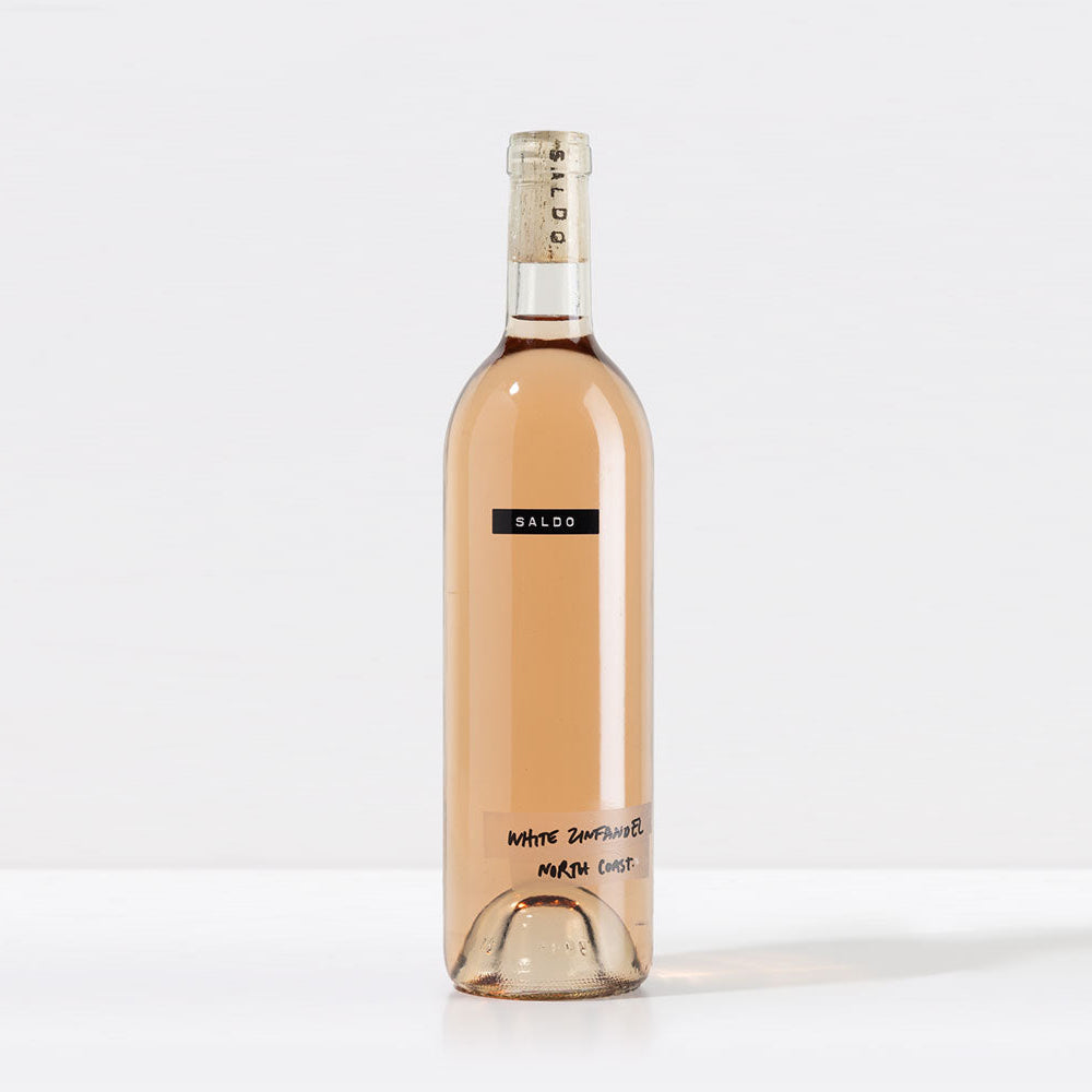 A bottle of 2023 SALDO White Zinfandel wine with a pink label and a clear bottle showing the light pink hue of the wine inside.