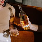 Person holding a bottle of SALDO Falanghina with a glass, sitting on a couch.