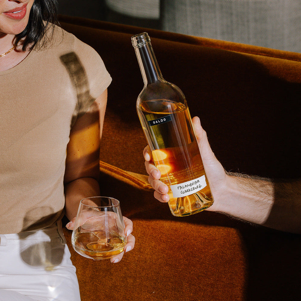 Person holding a bottle of SALDO Falanghina with a glass, sitting on a couch.
