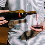 Person pouring red wine from a bottle into a glass, wearing a striped shirt.