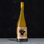 A bottle of the Winemaker Series Sweet White wine with a detailed black, red, and gold label, standing on a gray surface against a dark textured background.