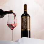 Red wine being poured into a glass with a bottle of Unshackled Cabernet Sauvignon in the background