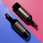 Two bottles of Unshackled Cabernet Sauvignon with gold labels on a pink and blue background
