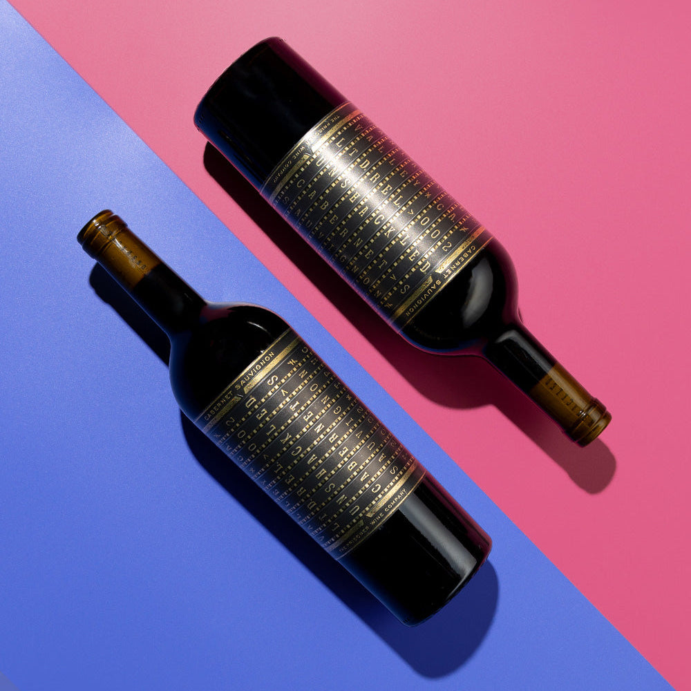 Two bottles of Unshackled Cabernet Sauvignon with gold labels on a pink and blue background